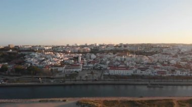 Portekiz 'in Algarve bölgesinde gün batımında beyaz binalar ve uzun nehir manzaralı bir şehir manzarası.
