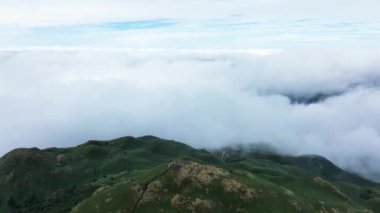 Bulutlarla dolu yeşil bir dağın tepesinden drone atışı.