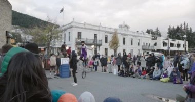 A street performer juggling fire sticks on a unicycle and entertaining a crowd in Queenstown