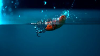 A slow-motion footage of an artificial bobber connected to a hook and falling into the water