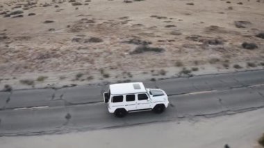 Beyaz bir Mercedes G Wagon çölde sürüyor.