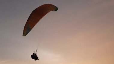 A tandem paraglider is paragliding over the ocean and lands on a hill top, where they took of before. This is a new leisure activity at Parangtritis.
