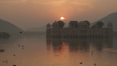 A beautiful shot of the Jal Mahal palace in the middle of Man Sagar Lake in Jaipur, Rajasthan, India with birds flying during sunrise