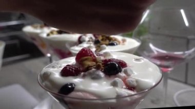 A closeup of a person decorating a cocktail dessert with raspberries and walnuts