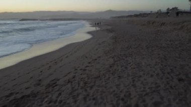 Fascinating drone view of the sea sandy beach, people walking along the shore and beautiful waves during sunset
