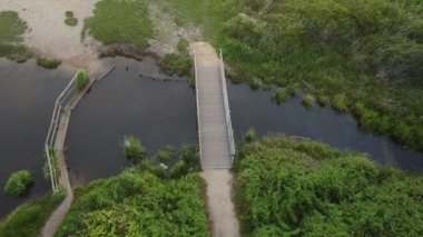 An aerial slow movement around greenery field with wooden bridge near road during sunset