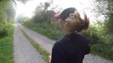 A side shot of a young female with a black sportive outfit running in narrow road between trees