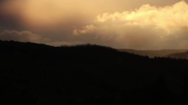 Parlak güneş ışığı altındaki dağların manzaralı görüntüsü yoğun kasvetli bulutların arasından ışıldıyor.