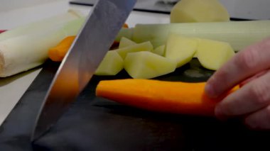 A cutting board with vegetables and a knife cutting carrot in slow motion