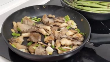 The closeup footage of the oyster mushrooms and Asparagus on the black frying pans.