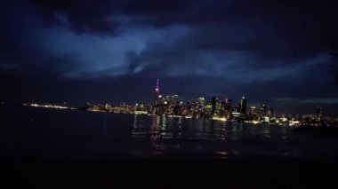 A view of the CN Tower in Toronto, Canada from Centre Island with the cloudy sky getting darker at night