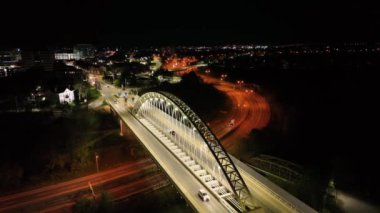 A drone shot over a bridge with cars on it and the cityscape with the city's lights at night