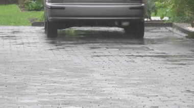A back view of a car parked near the park  and the rain pouring down on the cobblestone street