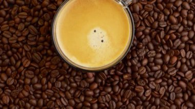 An overhead shot of a rotating cup of coffee on a pile of coffee beans