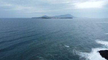 An aerial view of a beautiful seascape with calm waves against a cloudy sky