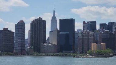 A sunny day with a bright cloudy sky over cars driving on a bridge above a lake in a big city