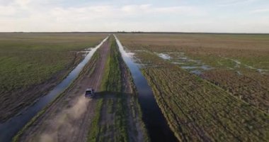 Aerial view of a blue truck by a dirt truck in the middle of the field, at the edge of a stream.