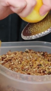 the close-up vertical shot of female hands grating lemon zest into a bowl of cereal