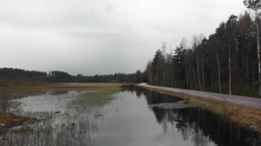 An aerial view of a small road with cyclists riding through a mossy lake and a forest in Falun, Sweden