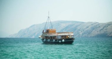 Arka planda dağlar olan mavi deniz manzaralı bir gemi manzarası.