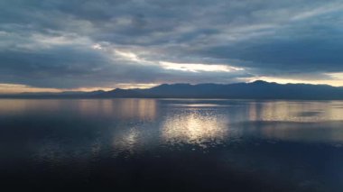 A gorgeous aerial view of the dark blue sunset at the Salton Sea in California with gentle golden lights shining onto the water from the cloudy sky