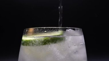 A closeup of water pouring into a glass with a slice of lime