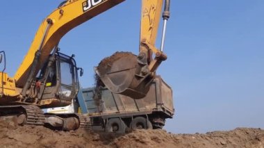 Bir Excavator toprak moorum kesiyor ve bir çöp kamyonuna yüklüyor..