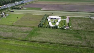 A bird's eye view of a building with a parking lot surrounded by green fields near a highway