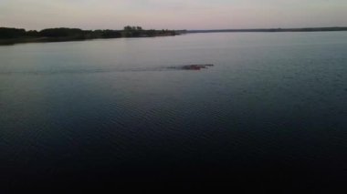 A drone footage of a lake and coastline with trees during sunset