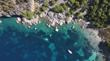 An aerial view of a boat in a bay with forested cliffs on the shore
