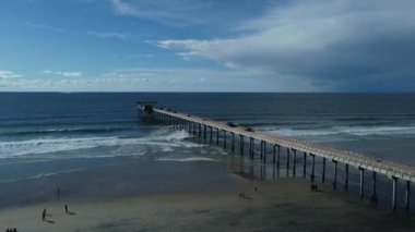A Drone shot La Jolla Shores with wavy ocean and a view of coastal houses under a blue cloudy sky