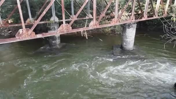 古い錆びたトラスの鉄の棒がインドの川の水を溢れさせて立っているインドの川の上の解体された橋の錆びたトラスの上を飛んでいる — ストック動画