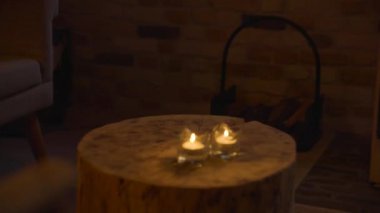 Two lighting candles on a tree stump using as a table near a fireplace in a wooden cabin in Elburg, Netherlands.