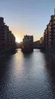 A vertical view of a river passing through buildings during sunset