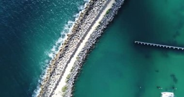 An aerial view of boats parked on a beach and cars parked on a rocky road inside the water with seascape on a sunny day