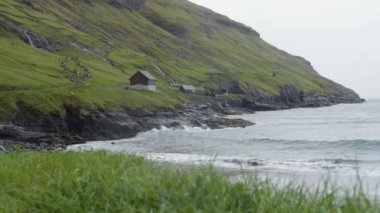 A body of water with the waves hitting the beach by hills and a small cottage