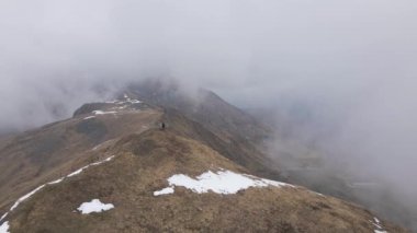 A top view of a hiker on the top of snow covered mountain under foggy clouds