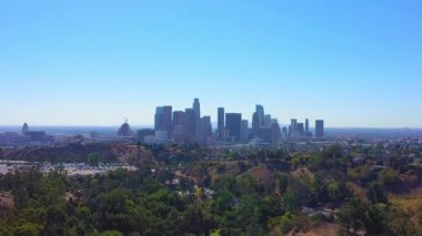 A gorgeous skyline of Los Angeles with lush green trees and proud skyscrapers under a clear, bright blue sky