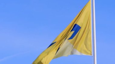 Waving flag of the Dutch National Railway company with logo in blue on a yellow banner in strong wind contrasted against clear blue sky