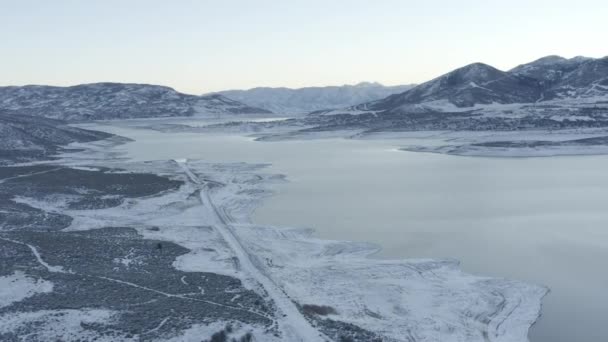 雪に覆われた山に囲まれた凍った湖の周りの空中スローモーション — ストック動画