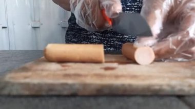 A person slicing salami on a wooden cutting board