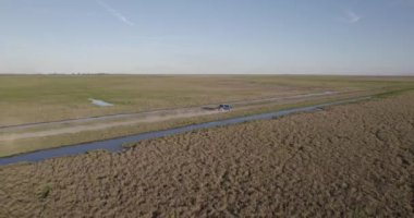 Aerial view of a blue truck by a dirt truck in the middle of the field, at the edge of a stream.