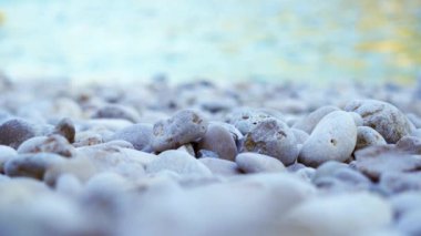 A selective focus on gray pebbles on the shore with moving water in the background