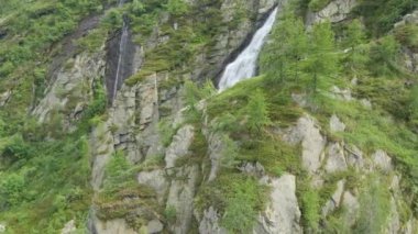 A drone shot over a beautiful waterfall flowing between green rocky mountains