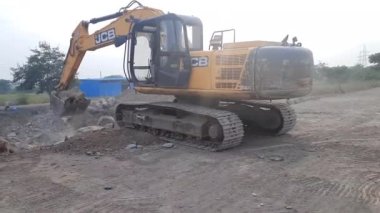 Toprak taşıma ekipmanları. Sarı kazıcı toprağı kazıyor. Kazı kovası inşaat alanındaki büyük kayayı topluyor..