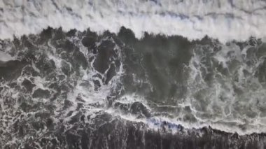 A drone shot of a wavy sea with a sandy beach