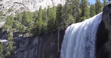 A beautiful waterfall coming down a tall hill with a rainbow on the rocks below