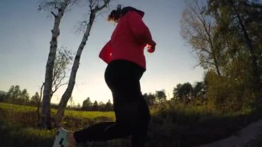 A low angle shot of a Caucasian female in a sportive outfit running through green meadows at sunset