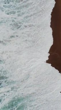 A vertical aerial drone footage of the big waves of washing the beach in Ericeira, Portugal