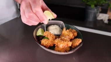 A chef squeezing lime on fried shrimp in a bowl